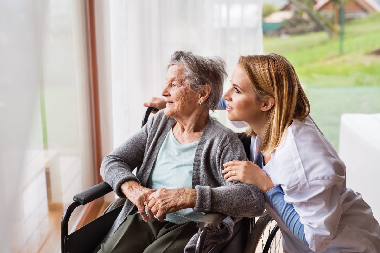 Pflegefachkraft im vertrauten Gespräch mit einer Seniorin am Fenster