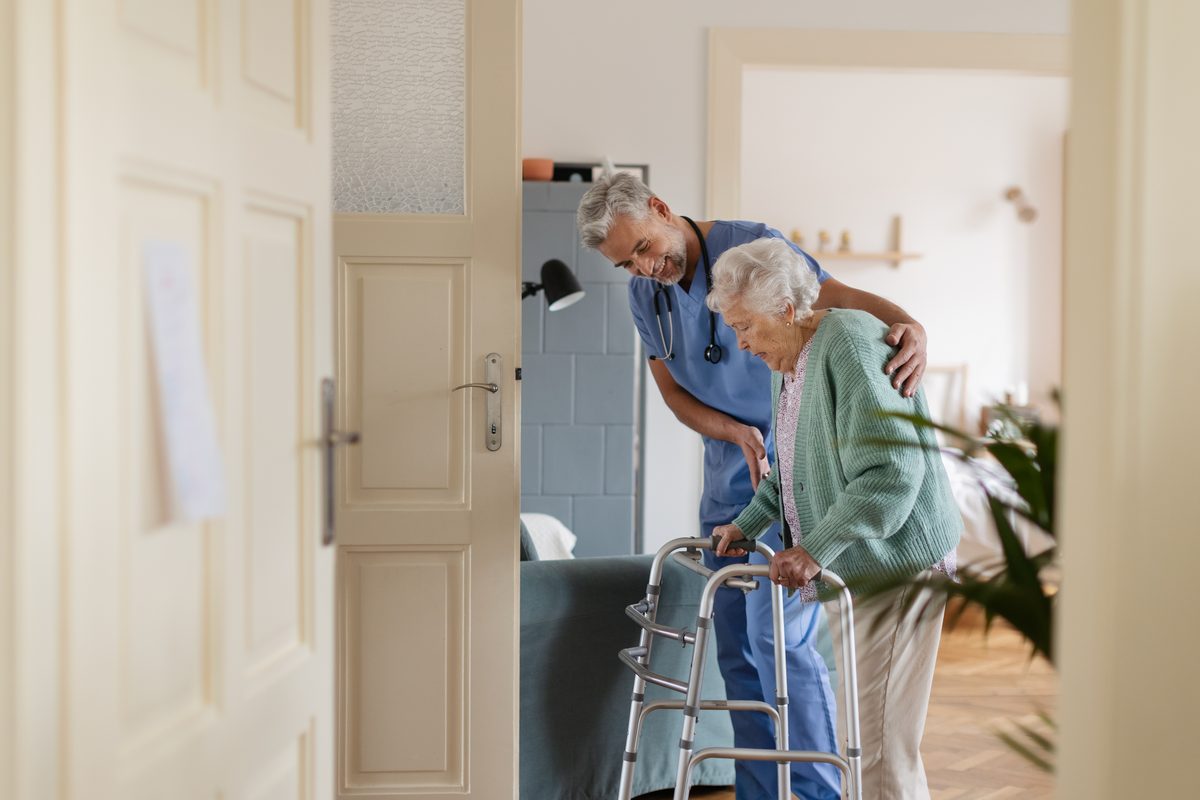 Pflegekraft begleitet einen Senior mit Rollator durch die Wohnung