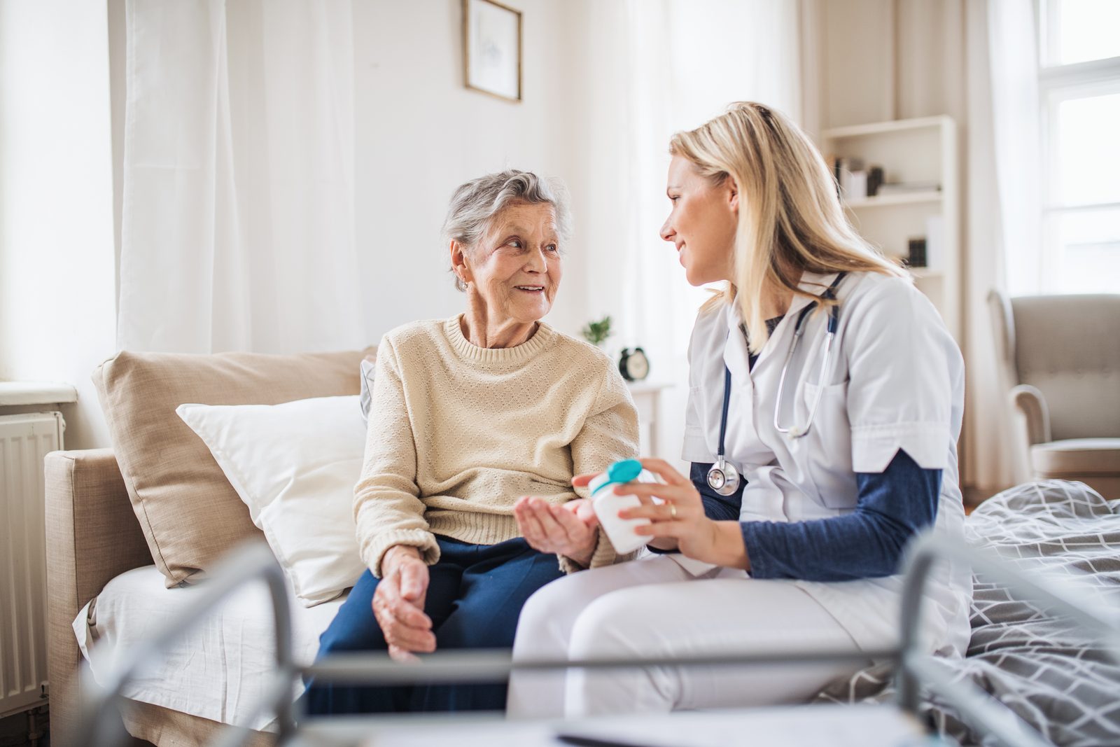 Pflegerin reicht einer Seniorin zuhause ihre Medikamente